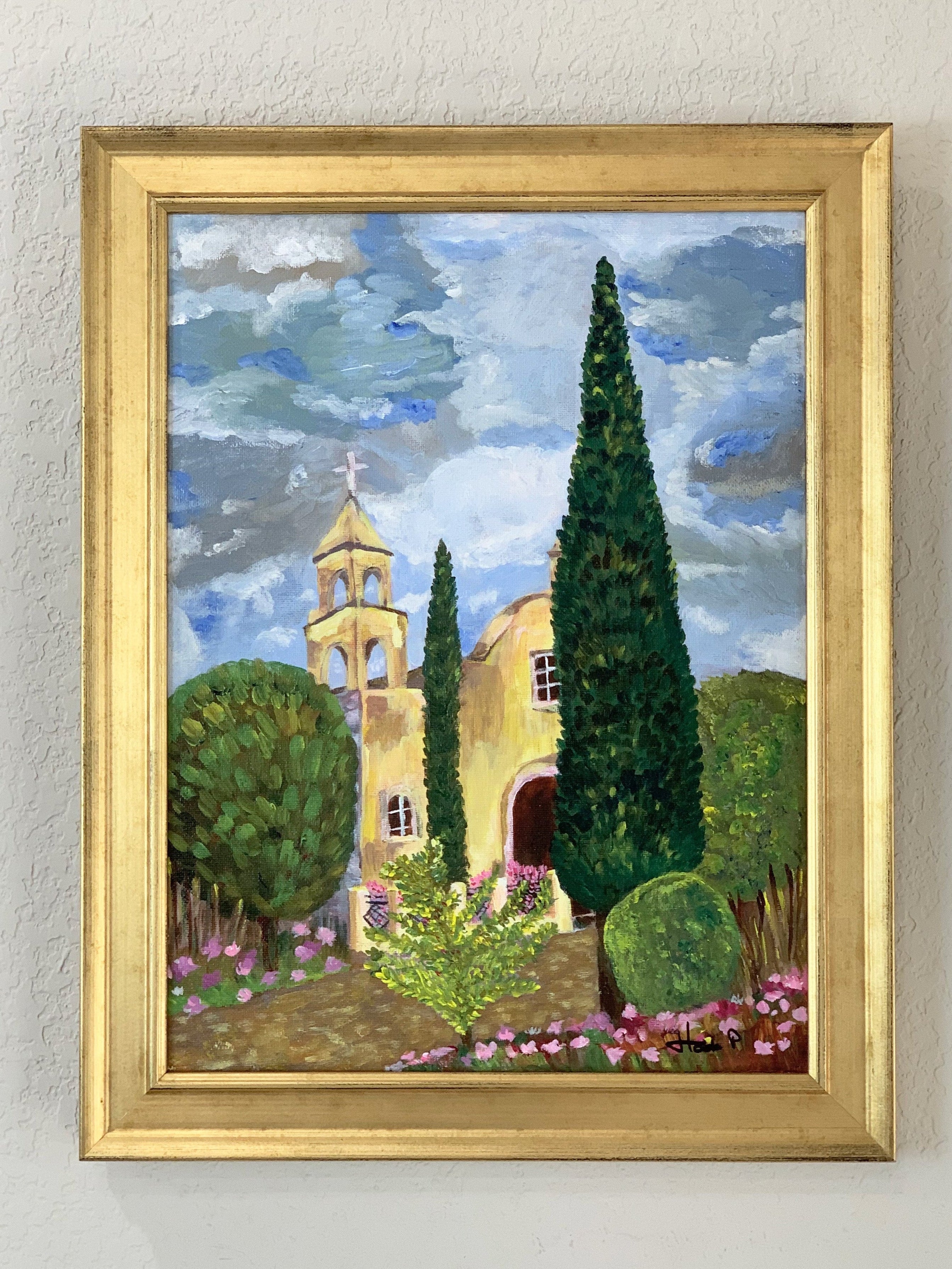Framed painting of a church with trees and flowers on a wall
