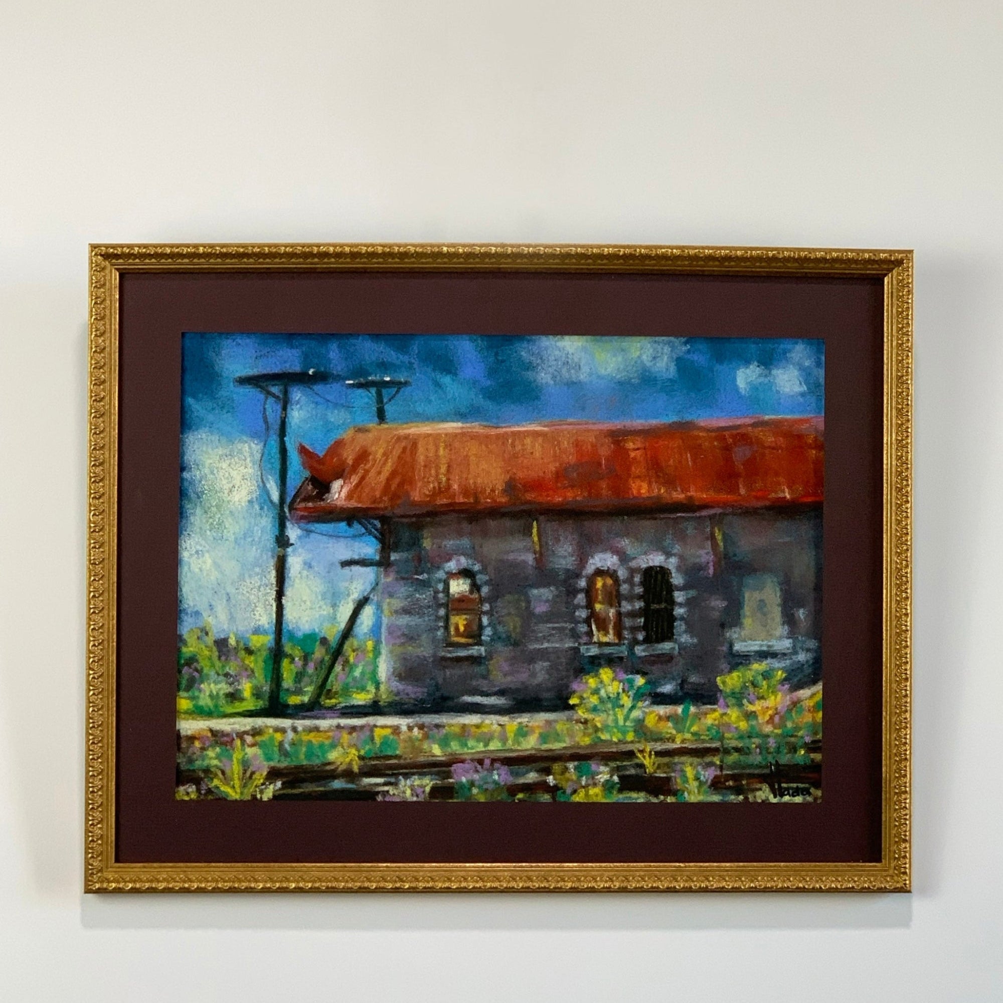 Framed painting of a rustic building with a rusted roof on a white wall
